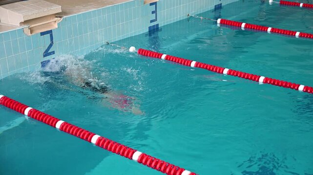 Female swimmer executes backstroke flip turn in indoor pool lane. Dynamic footage shows body rotation, wall approach, and powerful turn technique in blue water