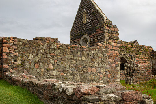 View of the ancient stone ruins of Iona Nunnery with weathered masonry walls and arched windows under a cloudy sky in Baile Mor, Scotland, United Kingdom.