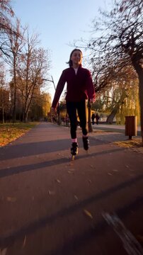 Girl skates on inline skates during sunset in open city space. Vertical shot captures evening fitness, freedom, and recreation on paved riverside walkway