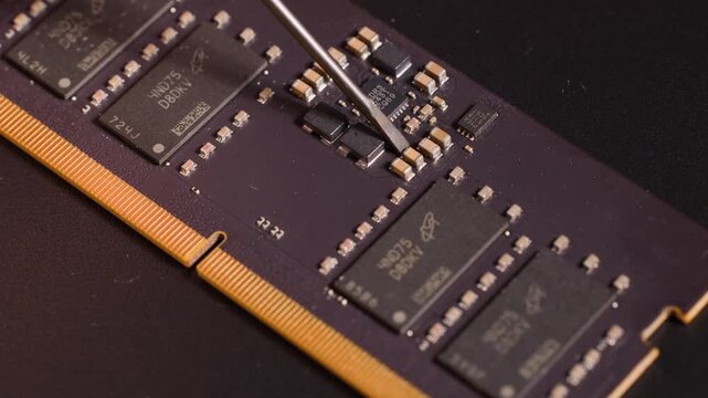 Close up of computer RAM module with skilled hand inspecting tiny components with tool.