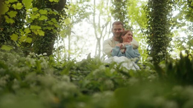 A happy couple enjoys a romantic embrace amongst wild garlic in sun-dappled woods.