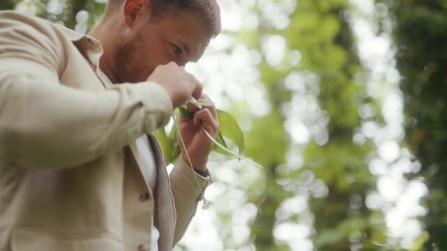 A man meticulously prepares fresh wild garlic greens outdoors in a lush natural setting.