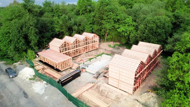 Aerial drone shot of wooden lodge complex under construction. Framed buildings and pool foundation reveal resort development in natural surroundings