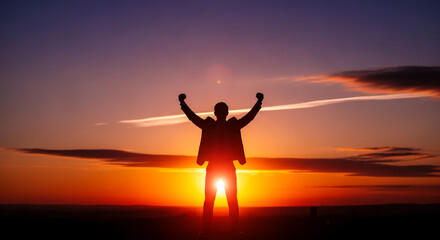 Fototapeta premium A triumphant man stands with arms raised at sunset outdoors freely