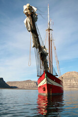 Red sailing ship in Skansbukta, Kongsfjorden, Svalbard, with rugged mountains and calm Arctic waters. © PYTeyssier