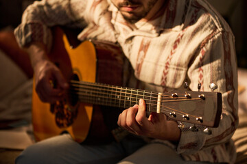 Obraz premium Young adult man playing acoustic guitar indoors, practicing chords and strumming strings for creative hobby, music learning, entertainment content, lifestyle marketing use