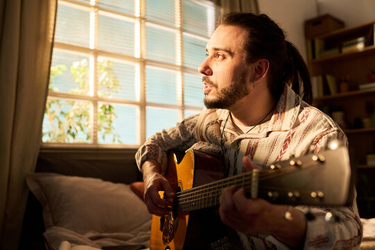 Young adult Caucasian man playing acoustic guitar and singing at home, practicing music and songwriting. Useful for creative hobby, home entertainment, musician lifestyle marketing