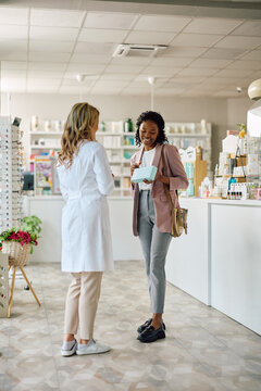 Happy black woman talking to pharmacist buying dermal care products in drugstore.