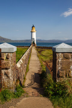 View of Tobermory Lighthouse at the end of a stone walkway framed by pillars with the sea and hills in the background in Isle of Mull, Scotland, United Kingdom.