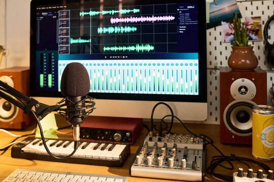 Close up of podcast microphone recording audio beside computer editing waveform tracks in home studio. Supporting content creation, voiceover production, streaming, marketing media