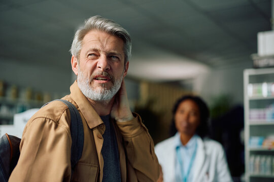 Mature man with headache in pharmacy looking away.