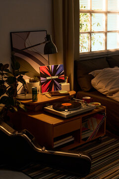 Vertical shot of bedroom corner featuring vinyl record player, rock album cover, guitar case, notebook, coffee cup, creating music hobby and home leisure concept for lifestyle marketing