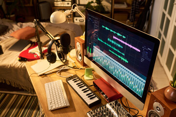 Fototapeta na wymiar Wide angle shot of home music production workspace showing audio editing software, microphone, headphones, keyboard, mixer. Supporting podcasting, content creation, remote studio marketing