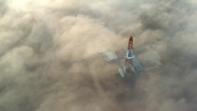 Aerial view of drilling rig partially covered by fog or dust over gas field.