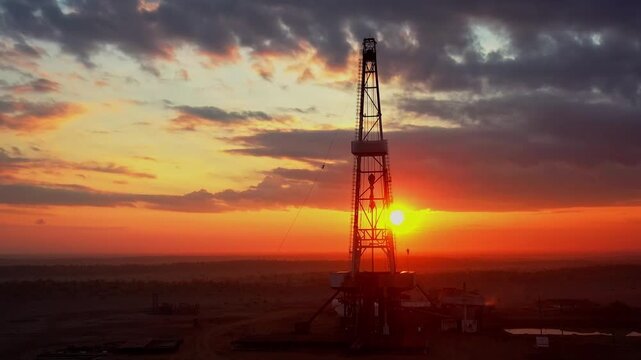 Industrial oil rig standing against colorful sunset sky in remote desert.