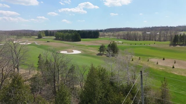 A drone ascends over TPC Osprey Valley, revealing fairways bordered by dense trees under a bright sky. Ideal for golf promotions or landscape features.