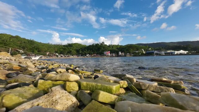 Timelapse of clouds moving above Romblon island with marble rocks in the beach foreground. Static camera captures tropical coastline textures sky motion and calm sea in the natural landscape.