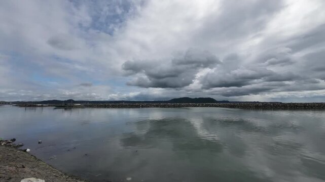 Timelapse of clouds moving over the ocean iloilo city with Guimaras Island in the background, Philippines. Static camera captures tropical seascape horizon motion and calm water on a cloudy day