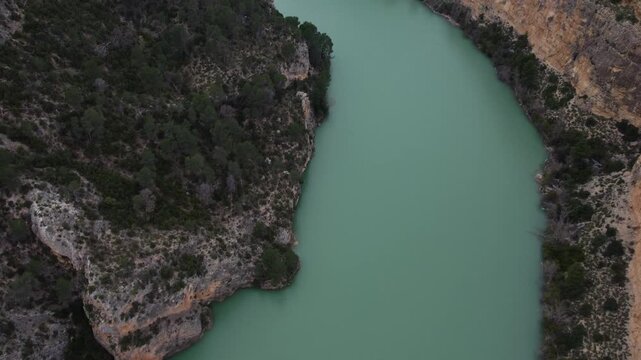 4K top-down aerial of the turquoise J&uacute;car River twisting through a massive canyon in Castilla-La Mancha, Spain. Steep limestone cliffs and lush green vegetation line the banks