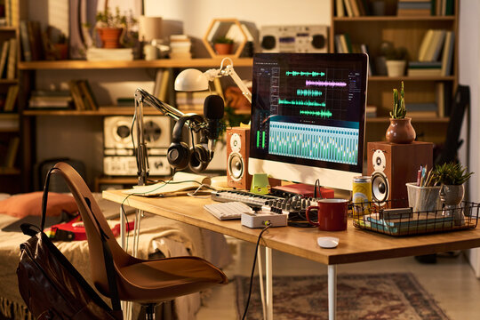 Wide shot of home podcast studio featuring computer editing audio, microphone, headphones, mixer, speakers. Supporting content creation, streaming, remote media production