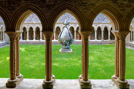 View of the cloisters of Iona Abbey and Nunnery featuring stone arches and a central sculpture in a green courtyard Isle of Iona, Scotland, United Kingdom.