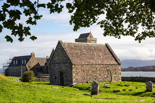 View of Iona Abbey and Nunnery with historic stone buildings and ancient graveyard overlooking the sea under a bright sky Isle of Iona, Scotland, United Kingdom.