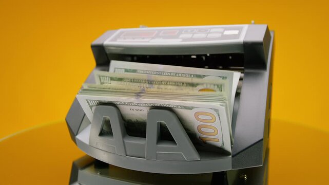 Dollar bills counted in money machine on yellow background