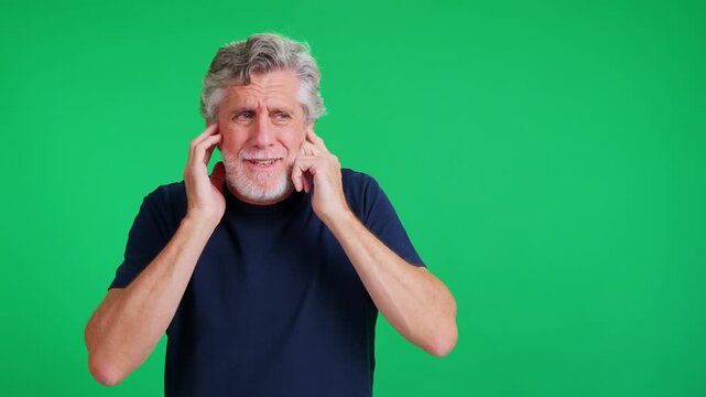 Stressed senior man plugging ears on a green screen