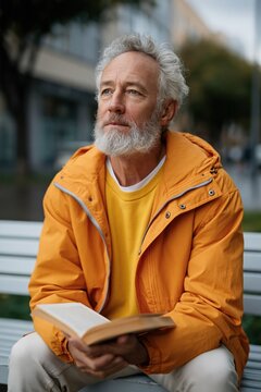 Senior man in orange jacket reading book on city bench