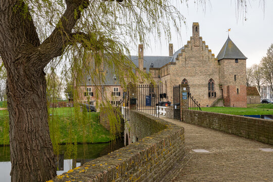 View of Radboud Castle with its historic brick walls and a stone bridge over the moat framed by a weeping willow tree in Medemblik, Noord-Holland, Netherlands.