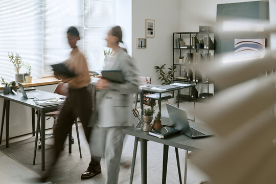 Wide shot of diverse businesswomen walking through office carrying folders, creating motion blur and teamwork concept. Ideal for corporate workflow, productivity, collaboration marketing