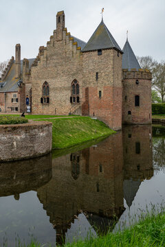 View of Radboud Castle with its medieval brick walls and towers reflecting in the calm water of the surrounding moat under an overcast sky in Medemblik, Noord-Holland, Netherlands.