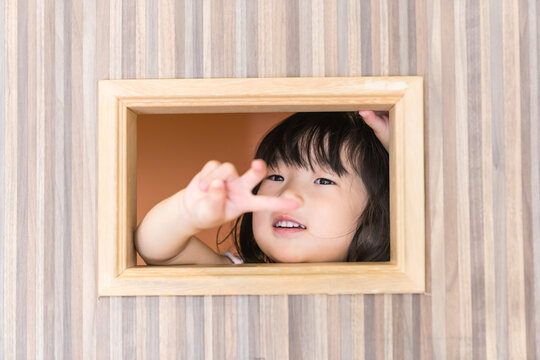 キッズルームの木枠の穴から満面の笑みでのぞく日本人の女の子の幼児