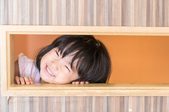 キッズルームの木枠の穴から満面の笑みでのぞく日本人の女の子の幼児
