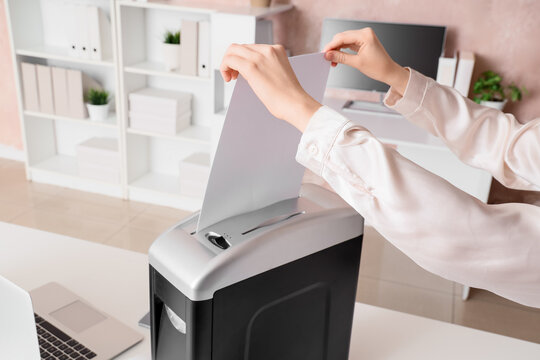 Female hands destroying document in shredder on desk at office