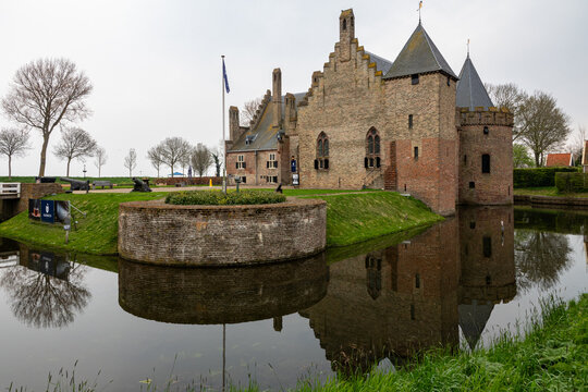 View of Radboud Castle with its brick walls and towers reflecting in the surrounding moat under an overcast sky Medemblik, Noord-Holland, Netherlands.