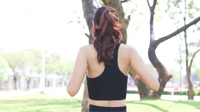 Young woman stretches arms outdoors. She smiles, enjoying nature. Trees and grass surround her. Sunlight filters through branches. Ideal for fitness or wellness themes. Gentle movement conveys calm
