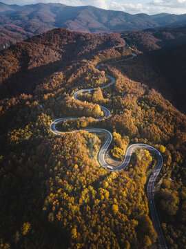 Cinematic aerial view of winding mountain road through colorful autumn forest landscape