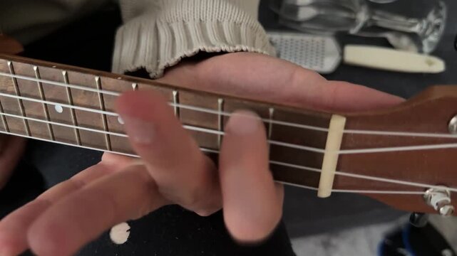 Man pressing strings on ukulele fretboard close up at home, playing chord, music practice moment, creative hobby activity, musical performance