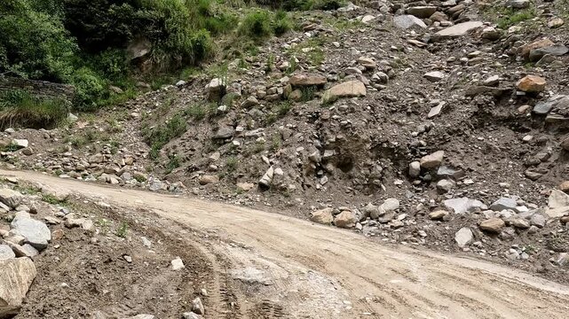 Rough mountain road passing through a rocky landslide-prone area with loose stones, mud & debris in a Himalayan landscape. Suitable for travel risk, mountain road conditions, , monsoon damage.