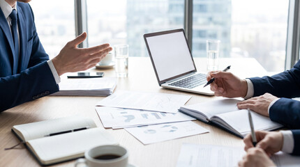 Business people's hands at an office desk, discussing strategy, with documents, laptop and coffee, bright. © Julie