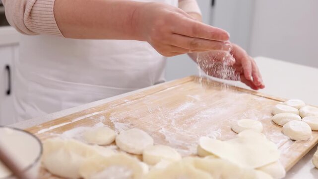 Unidentified hands senior woman baker chef wear apron sprinkles powdering raw flour piece of dough on table near a rolling pin prepare hands make dumpling from dough baking homemade pastry dessert