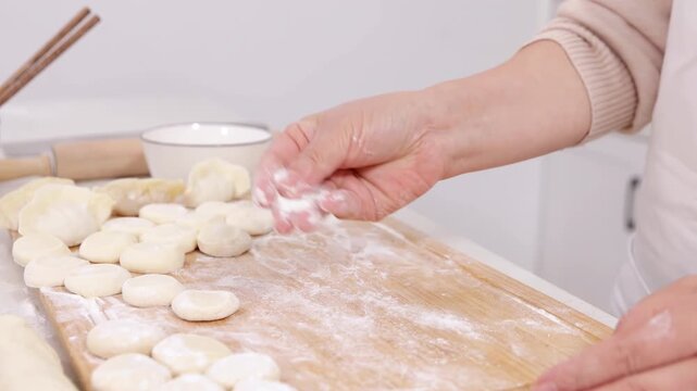 Unidentified hands elderly woman baker chef wear apron sprinkles flour a piece of dough on a table near a rolling pin prepare hands make dumpling from dough with meat on table, cooking hobby, leisure