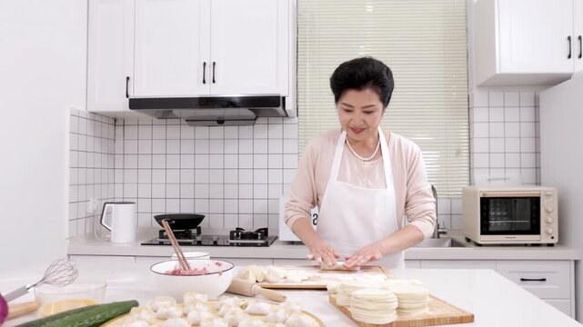 Portrait of elderly woman baker chef wear apron preparing dough flattening it with rolling pin for baking homemade pastry bakery food rolling dough on home kitchen table with raw fresh ingredients.