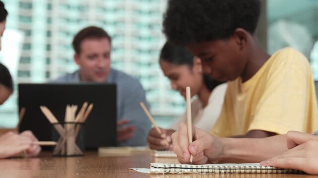 Closeup of student hand taking a note while girl ask teacher a question. Diverse student learning and study with smart happy instructor in classroom. Focus on hand. Creative education. Edification