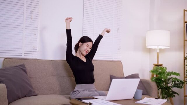 young Asian women stretching arms break from laptop computer remote work home office relaxing comfortable modern living room sofa wellness healthy workspace