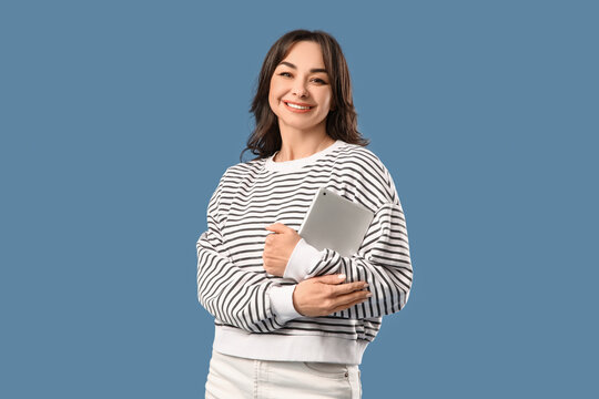 Beautiful woman with tablet computer hugging herself on blue background