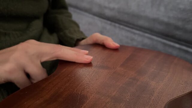 Person tapping fingers rhythmically on back of ukulele body close up at home, producing percussion sound, improvised music activity, creative hobby concept