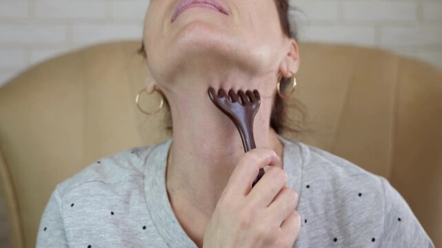 Woman performing neck massage with gua sha scraper tool. Caucasian woman massaging her neck with a gua sha tool, practicing a lymphatic drainage technique for anti-aging skin care, beauty rejuvenation