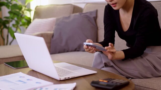 Asian businesswoman working from home office using laptop computer smartphone managing finance budget report professional young adult female multitask remote